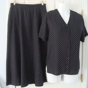 May include: A two-piece black skirt suit with a white polka dot pattern. The skirt is a long, straight style, and the short-sleeved top has a V-neck. The outfit is displayed on a white mannequin.