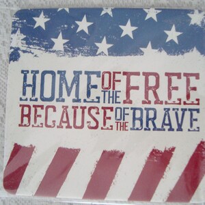 May include: Square coaster with a patriotic design. The top features a blue background with white stars and the text "HOME OF THE FREE BECAUSE OF THE BRAVE" in red and blue. Red and white stripes are at the bottom.