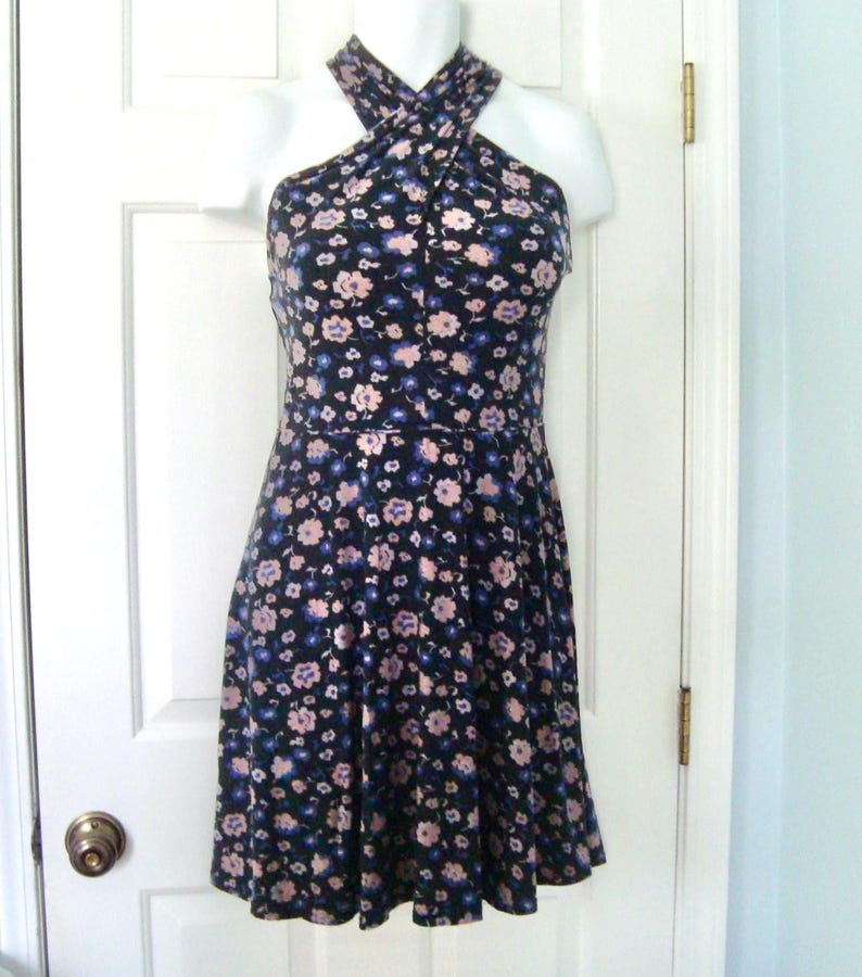 May include: A black halter dress with a floral pattern in shades of pink and blue. The dress is displayed on a white mannequin and features a fitted bodice and a flared skirt. The halter neckline crosses at the chest.