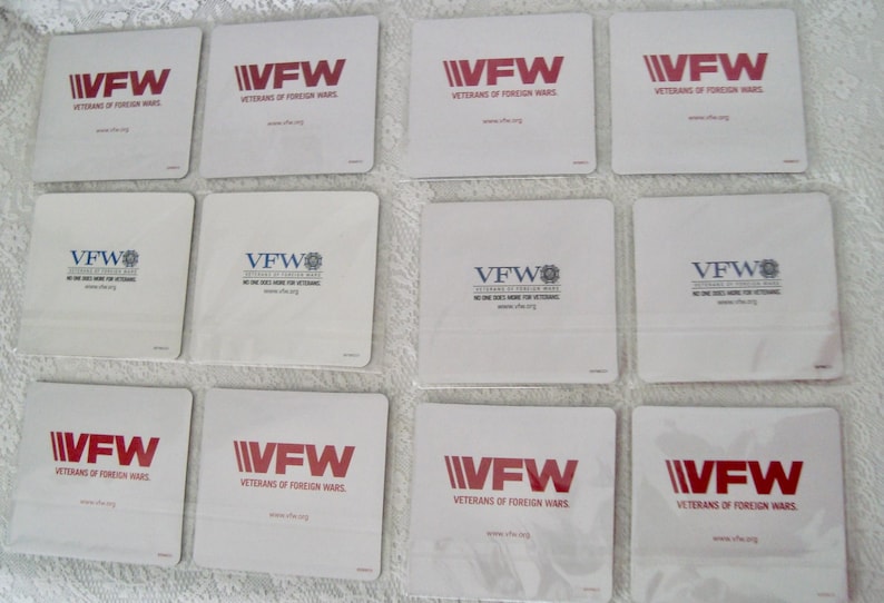May include: A collection of white square coasters featuring the VFW logo in red or blue. The text "VETERANS OF FOREIGN WARS" is printed below the logo. Some coasters also include the text "NO ONE DOES MORE FOR VETERANS."