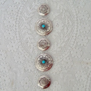 May include: Five silver-coloured metal buttons are displayed. Two buttons have a turquoise centre stone. The buttons feature a floral design with etched details. The buttons are arranged vertically against a white lace background.