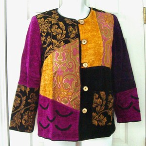 Puede incluir: Una chaqueta de manga larga con un diseño de patchwork de paneles de tela en negro, dorado y magenta. La prenda incluye un cuello redondo, cuatro botones de madera clara en la parte delantera y una mezcla de patrones florales y texturas lisas.
