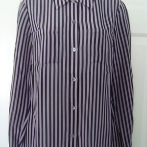 May include: A long-sleeve button-down shirt featuring a vertical striped pattern in shades of dark purple and black. The garment includes a standard collar, a front button placket with matching buttons, and two chest pockets on the front panels.
