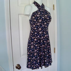 May include: A floral halter-neck dress. The dress has a dark navy blue base, adorned with small, scattered flowers in light pink and blue. The dress is displayed on a mannequin.