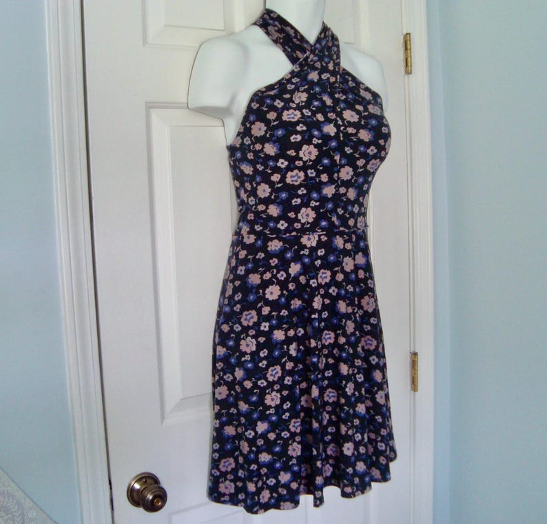 May include: A floral halter-neck dress. The dress has a dark navy blue base, adorned with small, scattered flowers in light pink and blue. The dress is displayed on a mannequin.