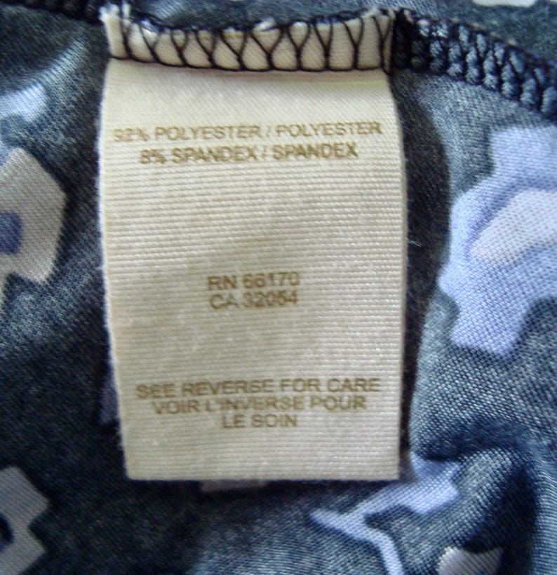 May include: A close-up shot of a fabric label. The label states "92% POLYESTER/POLYESTER 8% SPANDEX/SPANDEX", along with the codes "RN 66170" and "CA 32054". It also includes the text "SEE REVERSE FOR CARE VOIR L'INVERSE POUR LE SOIN".
