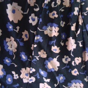 May include: Close-up of a dark fabric with a floral pattern. The design features small, stylized flowers in shades of light pink and blue against a dark background. The fabric appears to be soft and flowing, suitable for clothing.