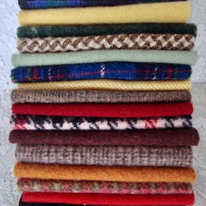 May include: A stack of various fabric swatches in a variety of colors and patterns. The swatches include shades of blue, yellow, green, red, and brown. Some have solid colors, while others feature plaid, herringbone, and other textured designs.