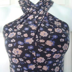 May include: A navy blue halter dress featuring a floral print in pale pink and blue. The dress is displayed on a white mannequin, highlighting the design and fit. The fabric looks soft and has a good drape.