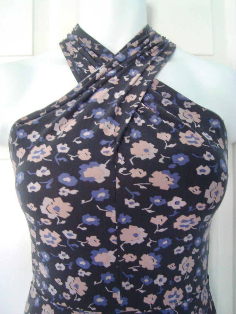 May include: A navy blue halter dress featuring a floral print in pale pink and blue. The dress is displayed on a white mannequin, highlighting the design and fit. The fabric looks soft and has a good drape.