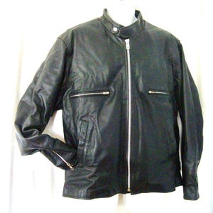 May include: A black leather jacket featuring a stand-up collar with a snap button closure, a full-length silver-tone front zipper, two horizontal zippered chest pockets, and zippered cuffs on the long sleeves, providing a classic and functional design.