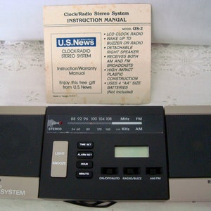 Puede incluir: Un radio reloj estéreo negro y beige vintage con un manual de instrucciones. La radio tiene un reloj LCD, radio AM/FM y un altavoz derecho desmontable. El manual es de U.S. News.