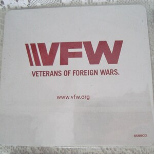 May include: A square, white coaster with the VFW logo in red. The logo includes the letters "VFW" and the words "Veterans of Foreign Wars." The website address www.vfw.org is also printed on the coaster.