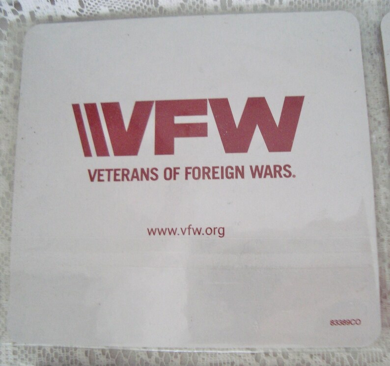 May include: A square, white coaster with the VFW logo in red. The logo includes the letters "VFW" and the words "Veterans of Foreign Wars." The website address www.vfw.org is also printed on the coaster.