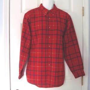 Può includere: Una camicia a maniche lunghe con bottoni caratterizzata da un colore di base rosso vivace con un motivo a griglia blu navy scuro e giallo sottile. La camicia include un colletto classico, un'abbottonatura frontale e maniche lunghe con polsini.