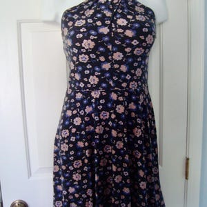 May include: A floral-print dress with a halter neck. The dress has a dark background with a pattern of small pink and blue flowers. The skirt flares from the waist, creating a flattering shape. The dress is displayed on a mannequin.