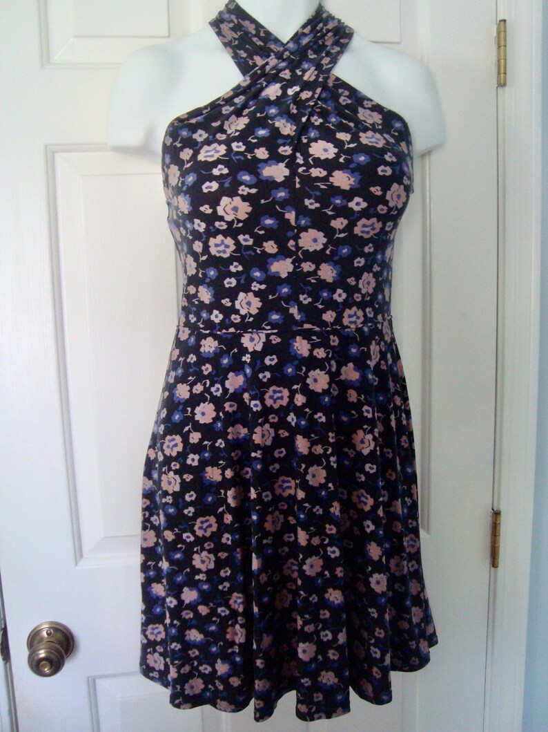 May include: A floral-print dress with a halter neck. The dress has a dark background with a pattern of small pink and blue flowers. The skirt flares from the waist, creating a flattering shape. The dress is displayed on a mannequin.