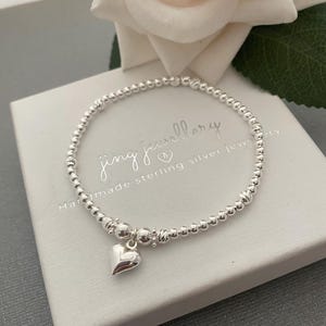 May include: A silver beaded bracelet with a small heart charm. The bracelet is on a white background with the text "Jing Jewellery Handmade sterling silver jewellery".