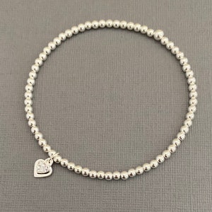 May include: A silver beaded bracelet with a small silver heart charm that has clear cubic zirconia stones.