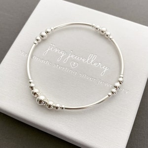 May include: A silver bracelet with small beads, on a white background. The bracelet is made of sterling silver and has a simple design. The text "jing jewellery handmade sterling silver jewellery" is printed on the background.