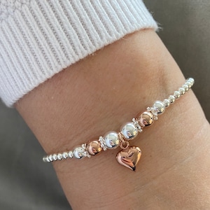 May include: A silver and rose gold beaded bracelet with a rose gold heart charm.