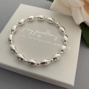 May include: A silver bracelet with oval-shaped beads. The bracelet is in a white box with the text "jing jewellery handmade sterling silver jewellery".