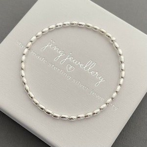 May include: A silver bracelet with small, round beads. The bracelet is on a white box with the text "jing jewellery handmade sterling silver jewellery".