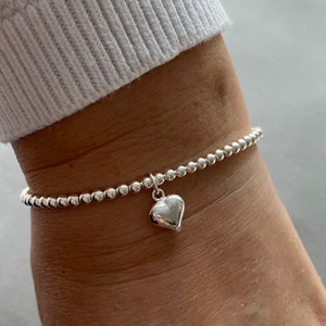 May include: A silver beaded bracelet with a small, silver heart charm.