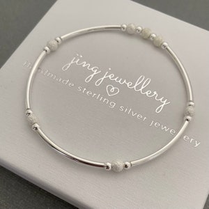 May include: A silver bracelet with small textured beads. The bracelet is on a white background with the text "jing jewellery handmade sterling silver jewellery".