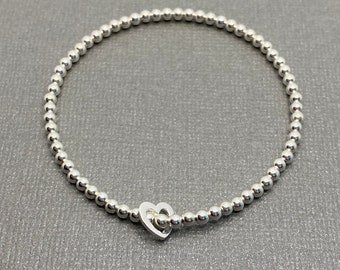 May include: A silver bracelet with a heart charm. The bracelet is made of small silver beads.