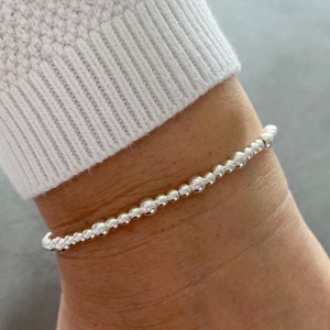 May include: A silver beaded bracelet with a simple design. The bracelet is made of small, round beads that are strung together on a thin chain.