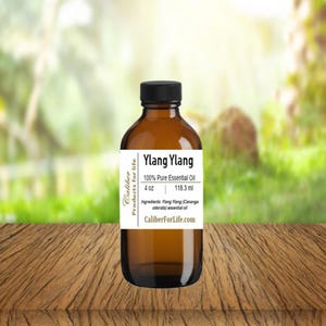May include: A 4-ounce amber glass bottle of Ylang Ylang essential oil. The label is white with black text and reads "Caliber Products for Life", "Ylang Ylang", "100% Pure Essential Oil", "4 oz", "118.3 ml", "Ingredients: Ylang Ylang (Cananga odorata) essential oil", and "CaliberForLife.com".