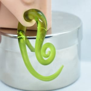 May include: A green glass spiral ear gauge plug. The plug is a single piece of glass that is twisted into a spiral shape.