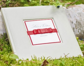 Puede incluir: Un álbum de fotos blanco con un lazo rojo y el texto "Dawn & Oliver 10.10.2015" en la portada.