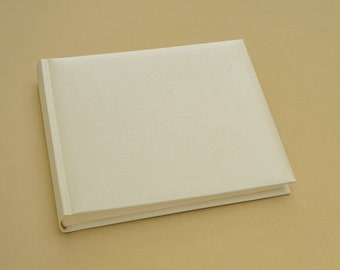 Puede incluir: Un libro blanco en blanco con una cubierta texturizada. El libro está acostado sobre una superficie beige.