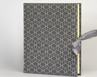 May include: A gray photo album with a geometric pattern and a gray ribbon tied around it.