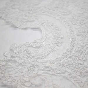 K&ouml;nnte beinhalten: Wei&szlig;e Spitzenborte mit einem zarten Blumenmuster. Die Spitze ist weich und flie&szlig;end, mit einem leicht gewellten Rand.