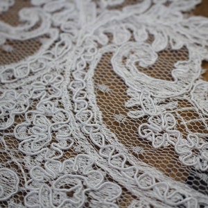 K&ouml;nnte beinhalten: Wei&szlig;er Spitzenstoff mit einem zarten Blumenmuster. Die Spitze hat ein erhabenes, strukturiertes Design und besteht aus einem feinen Netzmaterial.