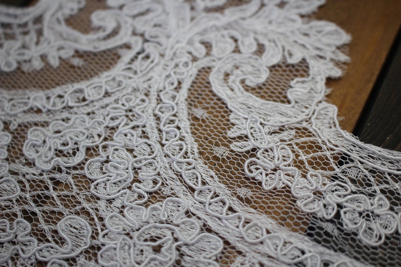K&ouml;nnte beinhalten: Wei&szlig;er Spitzenstoff mit einem zarten Blumenmuster. Die Spitze hat ein erhabenes, strukturiertes Design und besteht aus einem feinen Netzmaterial.