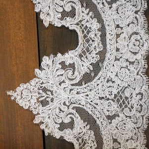 K&ouml;nnte beinhalten: Wei&szlig;e Spitzenborte mit zartem Blumenmuster. Die Spitze hat einen gewellten Rand und ist perfekt, um jedem Projekt einen Hauch von Eleganz zu verleihen.