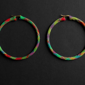 Op de afbeelding: Een paar grote creolen met een kleurrijk geometrisch patroon. De oorbellen zijn gemaakt van stof en hebben een gouden metalen sluiting.