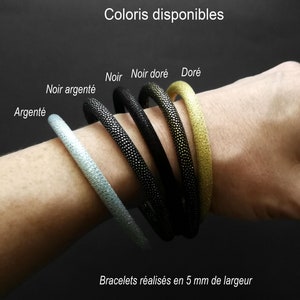 Peut inclure: Cinq bracelets de différentes couleurs : argent, noir, noir avec des paillettes dorées, or avec des paillettes noires et or. Les bracelets mesurent 5 mm de large et sont faits d’un matériau scintillant. "Coloris disponibles" et "Bracelets réalisés en 5 mm de largeur" sont écrits en français en haut et en bas de l’image.