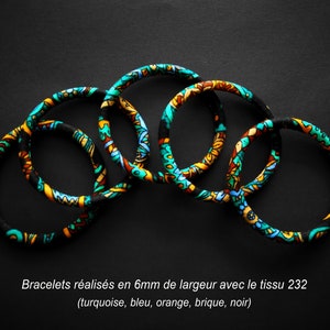 Peut inclure: Cinq bracelets en tissu colorés avec un motif turquoise, bleu, orange, brique et noir. Les bracelets mesurent 6 mm de large et sont disposés en cercle.