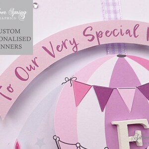 May include: A pink and purple hot air balloon banner with the text "To Our Very Special Niece" and the letter "F" in white. The banner is decorated with pink and purple pennants.