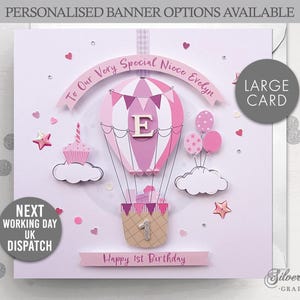 May include: A pink and white hot air balloon card with a banner that reads "To Our Very Special Niece Evelyn". The balloon has a pink and white striped pattern and a pink letter "E" in the center. The card also has a pink cupcake and a pink star. The card is decorated with glitter and rhinestones. The card reads "Happy 1st Birthday" and "Large Card".