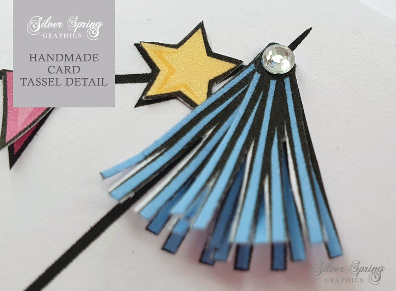 May include: A blue and black tassel with a white star and a rhinestone on top. The tassel is attached to a black stick. The text 'Handmade Card Tassel Detail' is in the background.