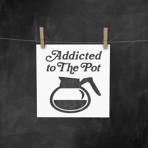 May include: A white sign with black text and a black silhouette of a coffee pot hanging on a clothesline with pegs. The text reads "Addicted to The Pot".