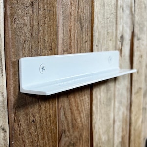 May include: A white metal shelf fixed to a wooden surface. The shelf is rectangular with a lip and is secured with screws. The wood has a natural, rustic appearance.