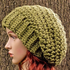 May include: A green crocheted slouchy beanie hat with a textured stitch pattern. The hat is worn on a mannequin with red hair.