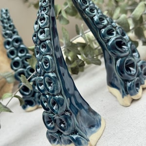 May include: Ceramic tentacle sculptures in shades of teal and blue, with a glossy finish. The tentacles have a textured surface with circular details and a cream-colored base. Decorative art.